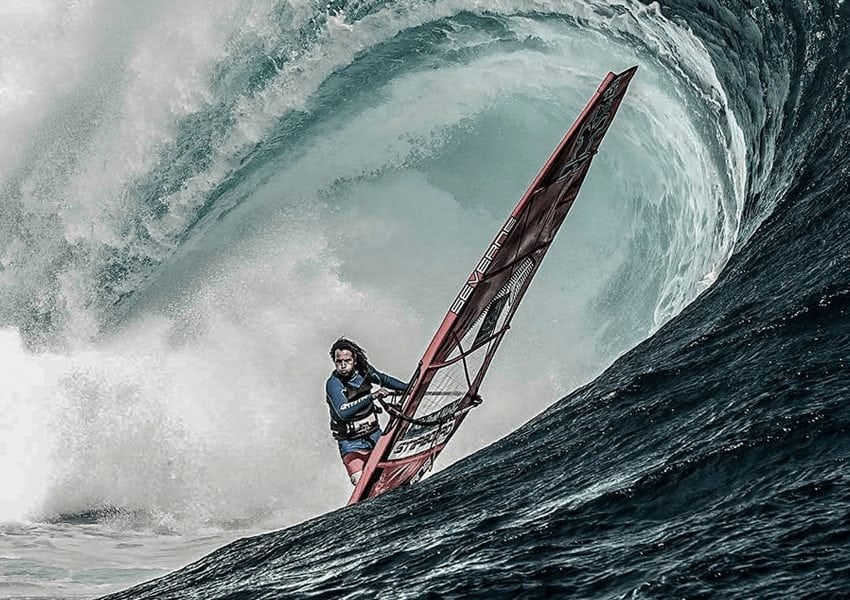 Man wind-surfing under huge wave